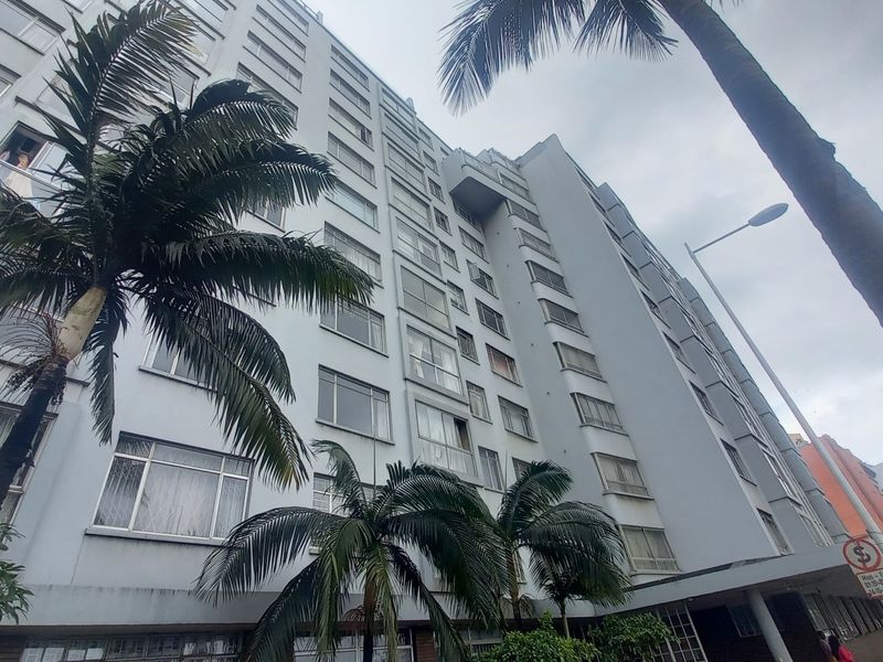 Low-angle view of a multi-story apartment building facade featuring numerous windows and surrounding palm trees.