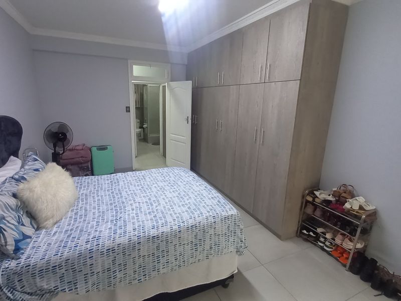 A spacious bedroom featuring extensive built-in cupboards, tiled flooring, and direct access to an en-suite bathroom.