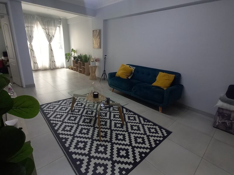 A bright and spacious living room featuring neutral tiled flooring and classic coved ceiling cornices, offering a clean and versatile living space.