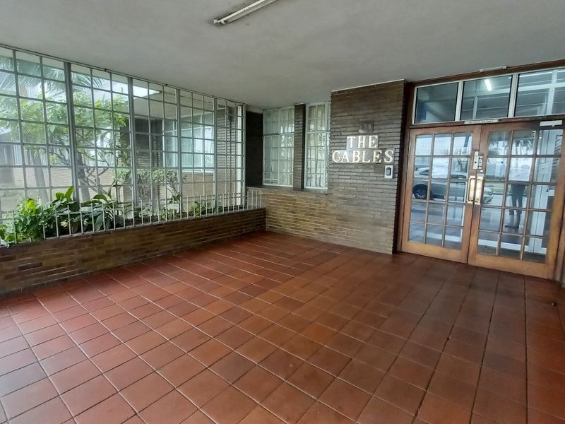 The entrance area of The Gables apartment complex features a covered tiled porch, brick facade, and secure double timber doors.