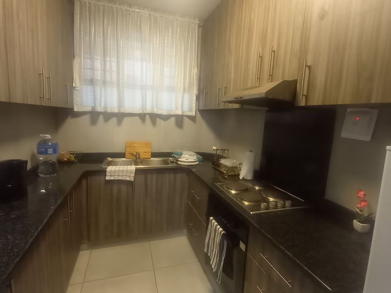 A functional kitchen featuring wood-look laminate cabinetry, dark granite countertops, a built-in oven, electric hob, and extractor fan with tiled flooring.