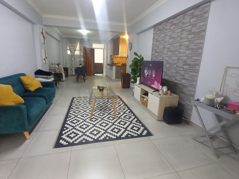 Spacious open-plan living area featuring neutral tiled flooring, decorative stone-effect wall cladding, and coved ceiling cornicing, creating a bright and functional living space.