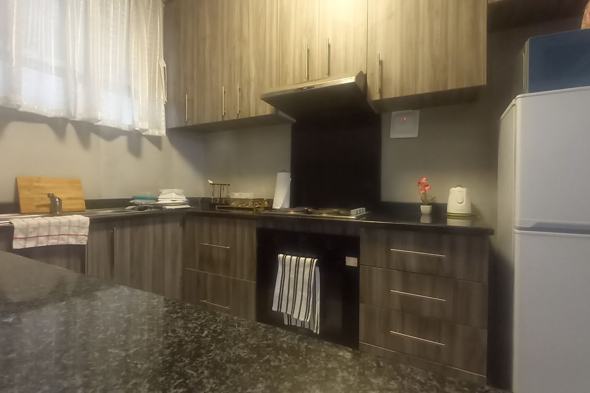 A functional kitchen featuring wood-grain cabinetry, dark granite countertops, a built-in oven, and an extractor fan.