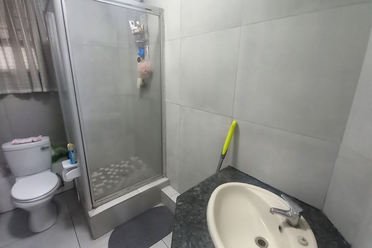 A functional bathroom featuring a shower enclosure, toilet, and a vanity basin with tiled finishes throughout.