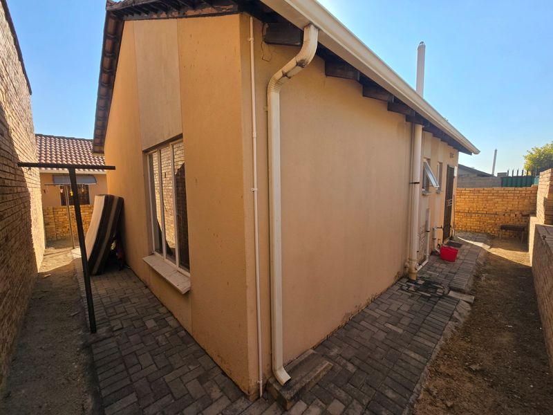 Rear exterior view of the townhouse featuring paved walkways, brick boundary walls, and visible exterior plumbing and guttering systems.