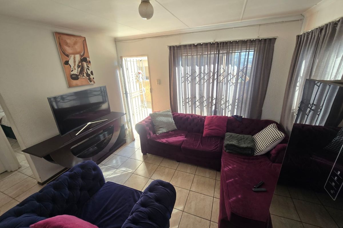A living room featuring tiled flooring, a sliding door with a security gate, and natural light, offering a functional space for relaxation.