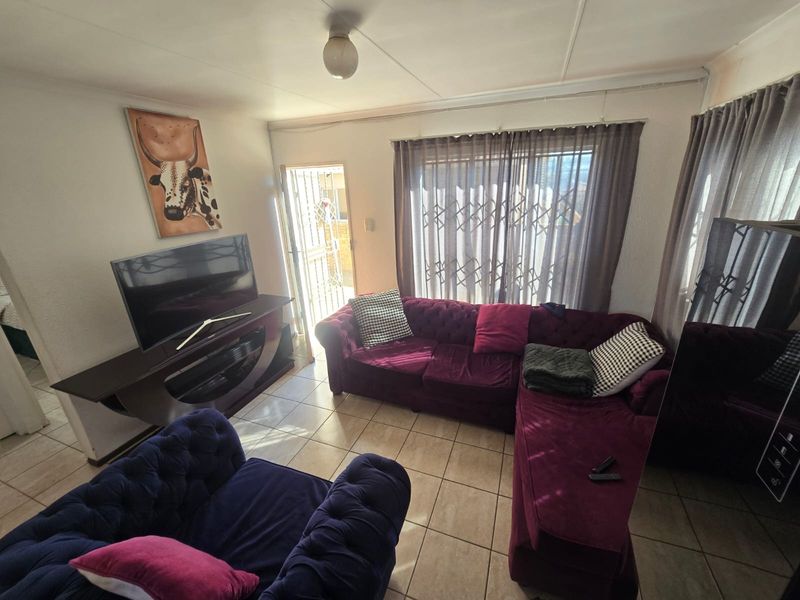 A living room featuring tiled flooring, a sliding door with a security gate, and natural light, offering a functional space for relaxation.