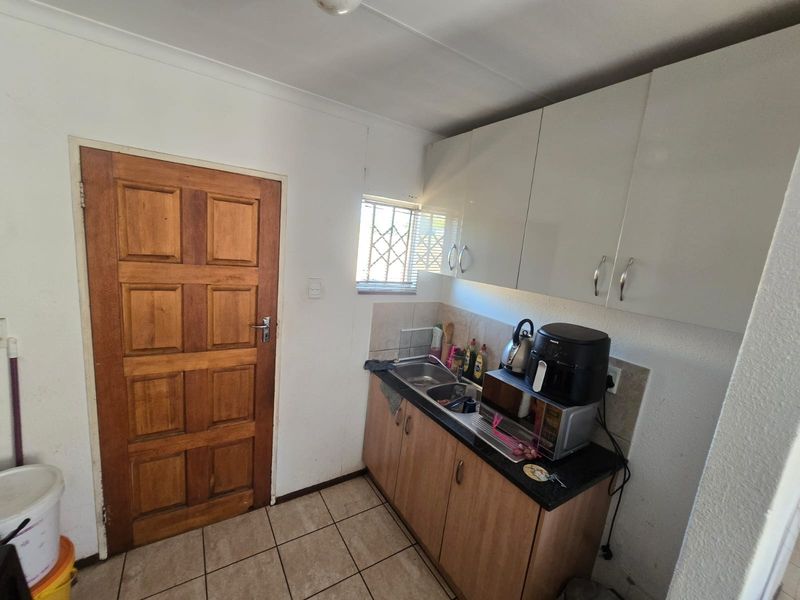 Compact scullery area featuring built-in cabinetry, a stainless steel sink, and tiled flooring, providing functional utility space for the home.