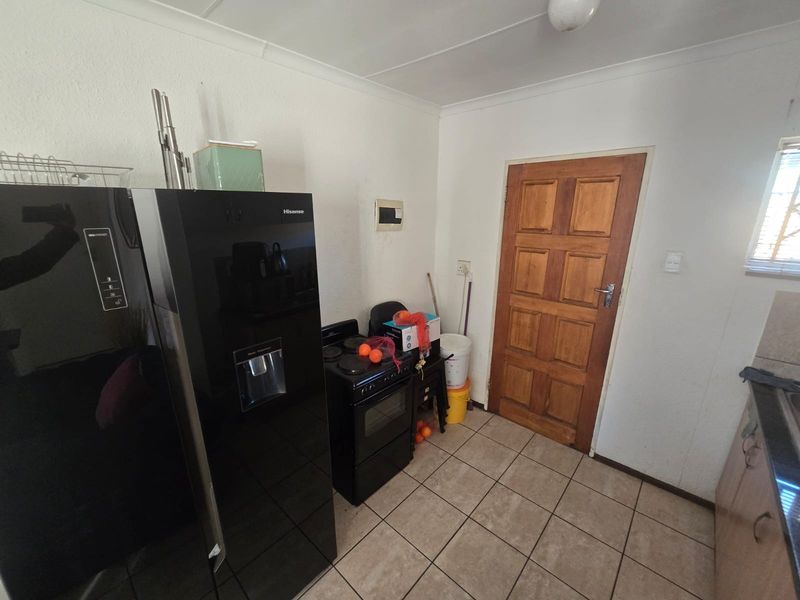 A functional kitchen area featuring tiled flooring, a wooden door, and basic cabinetry, offering potential for modernization and aesthetic improvement.