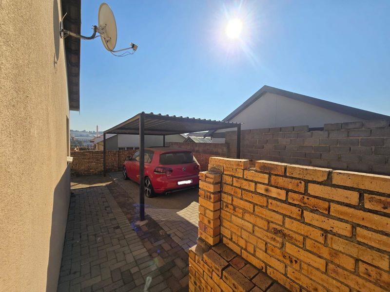 Rear exterior area featuring a paved driveway, a metal carport structure, and brick boundary walls.