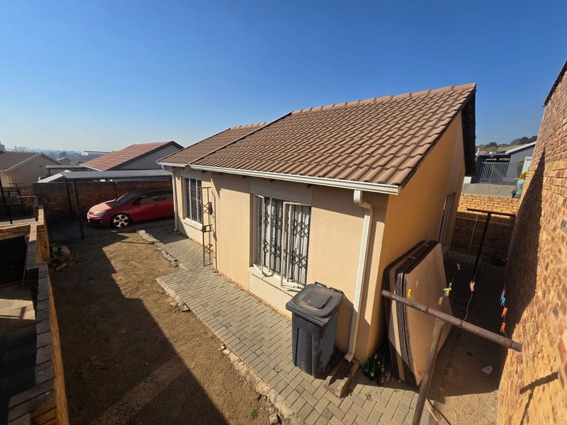 Rear view of the townhouse featuring a tiled roof, paved walkway, and brick boundary walls, with access to a small garden area.