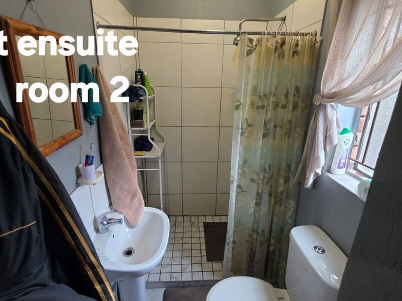 A compact ensuite bathroom featuring a pedestal sink, toilet, and a tiled shower area with a curtain.