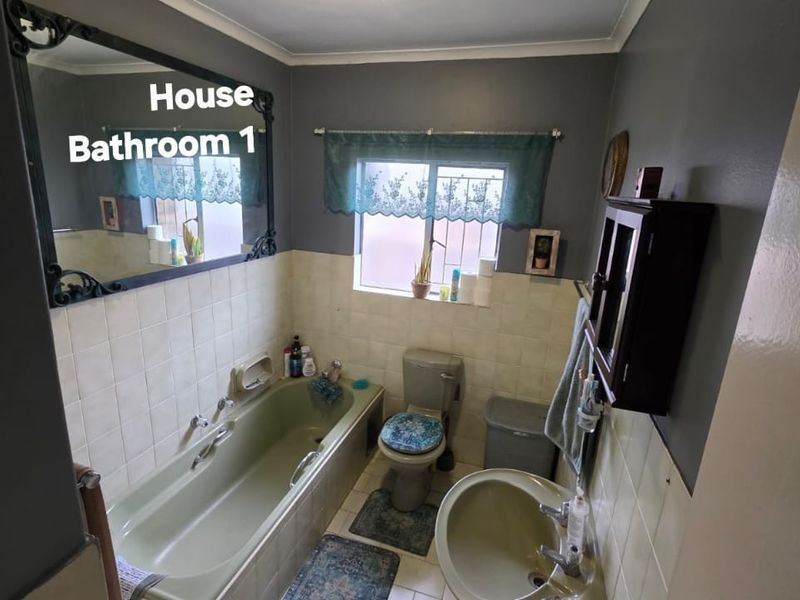 A functional bathroom featuring a bathtub, pedestal basin, and toilet with tiled splashbacks and a large wall-mounted mirror.