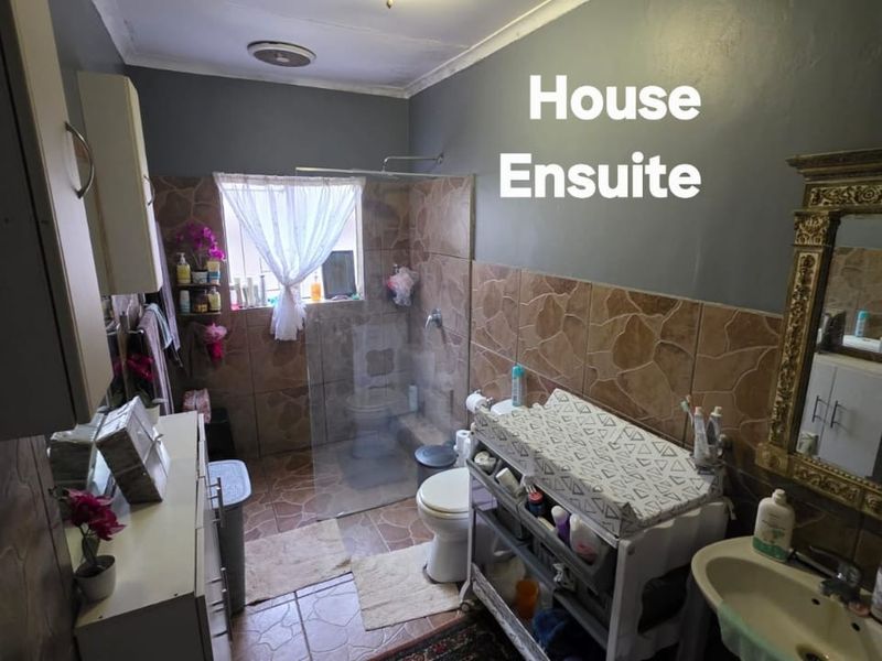 A functional ensuite bathroom featuring a walk-in shower with glass screen, pedestal basin, and toilet, finished with decorative ceramic wall and floor tiling.