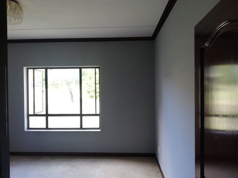 A clean, empty bedroom featuring neutral grey walls, dark wood trim, and a large multi-pane window providing natural light.