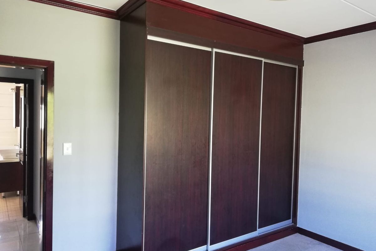 A bedroom featuring a large, dark wood built-in wardrobe with sliding doors and matching crown molding, leading to an adjacent bathroom.