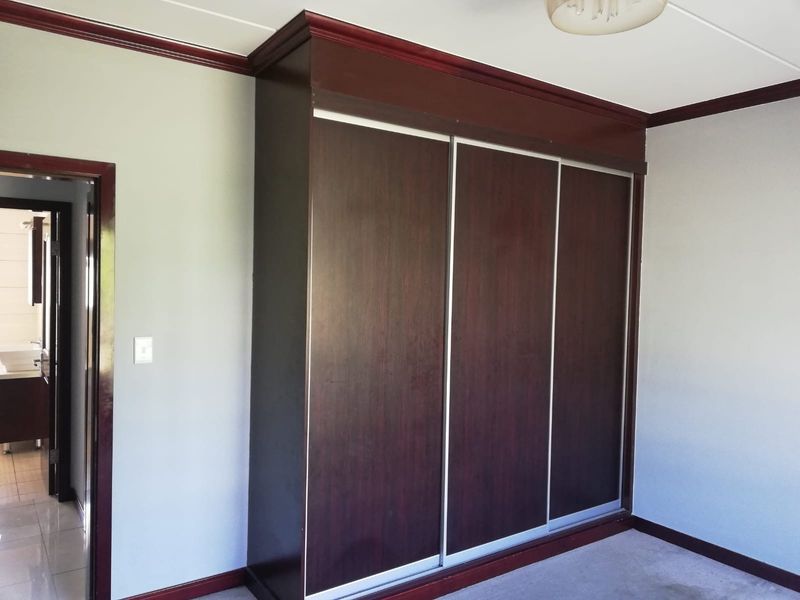 A bedroom featuring a large, dark wood built-in wardrobe with sliding doors and matching crown molding, leading to an adjacent bathroom.