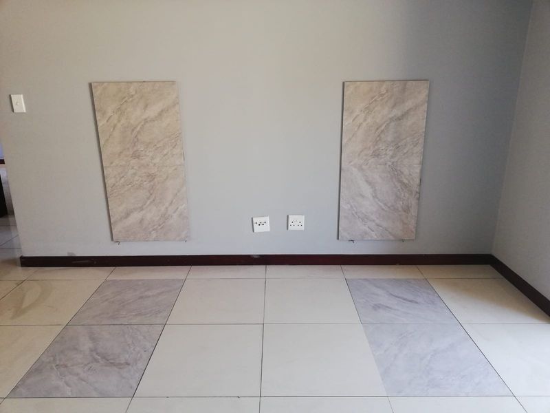 An empty living area featuring neutral ceramic floor tiles and wall-mounted decorative panels with integrated electrical points.