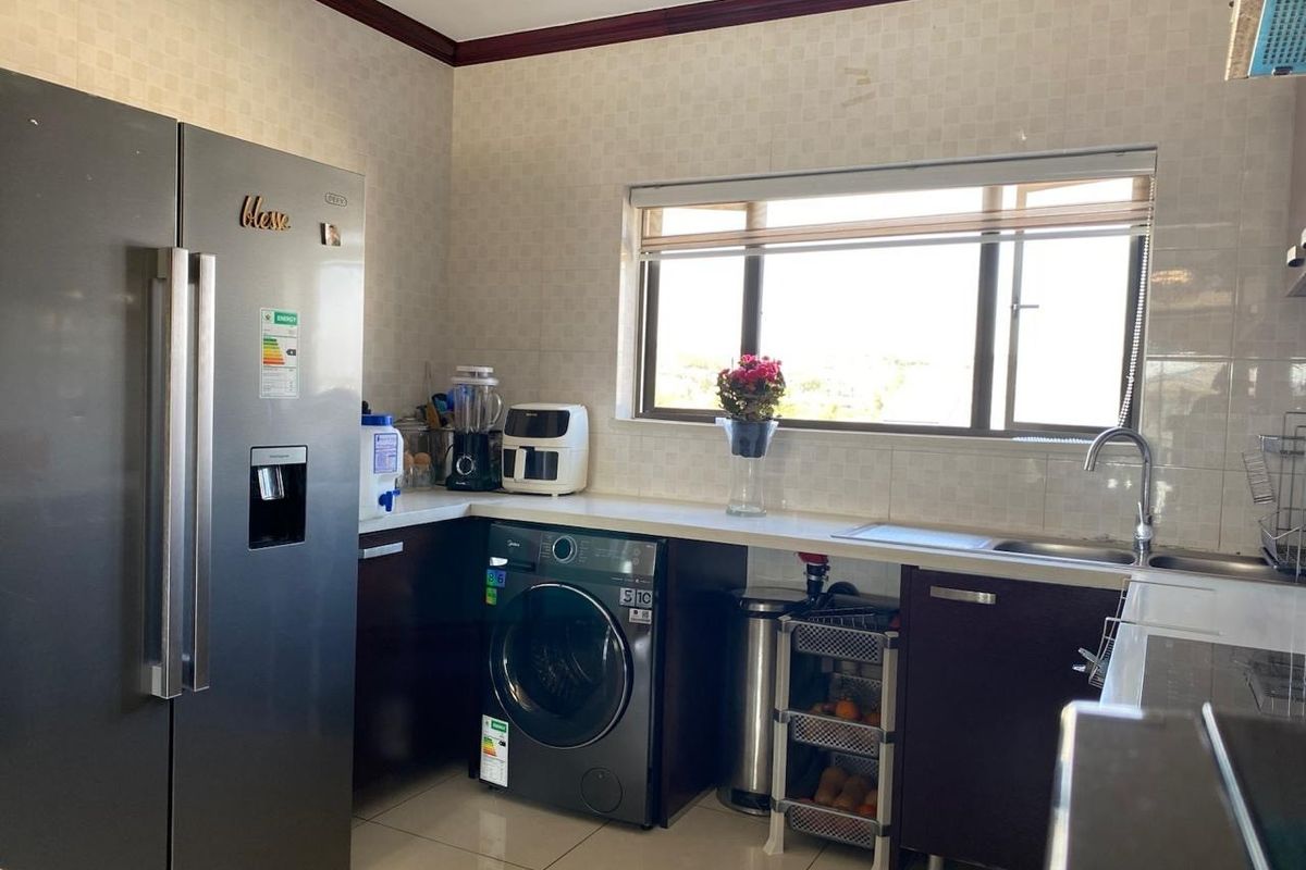 A functional kitchen featuring dark cabinetry, tiled backsplash, a stainless steel sink, and tiled flooring with natural light from the window.