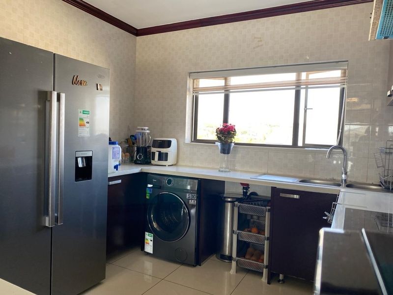 A functional kitchen featuring dark cabinetry, tiled backsplash, a stainless steel sink, and tiled flooring with natural light from the window.