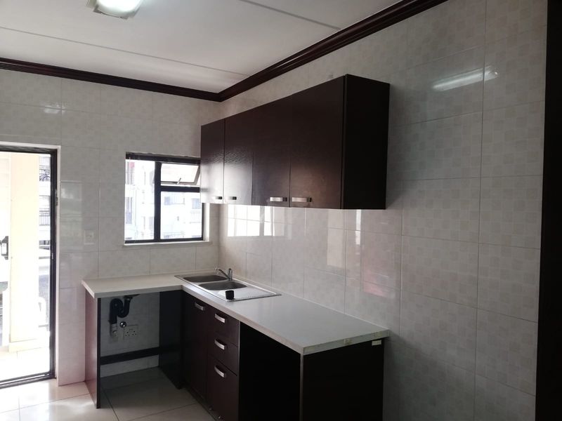 A functional kitchen featuring dark wood cabinetry, light laminate countertops, a stainless steel double sink, and full-height wall tiling.