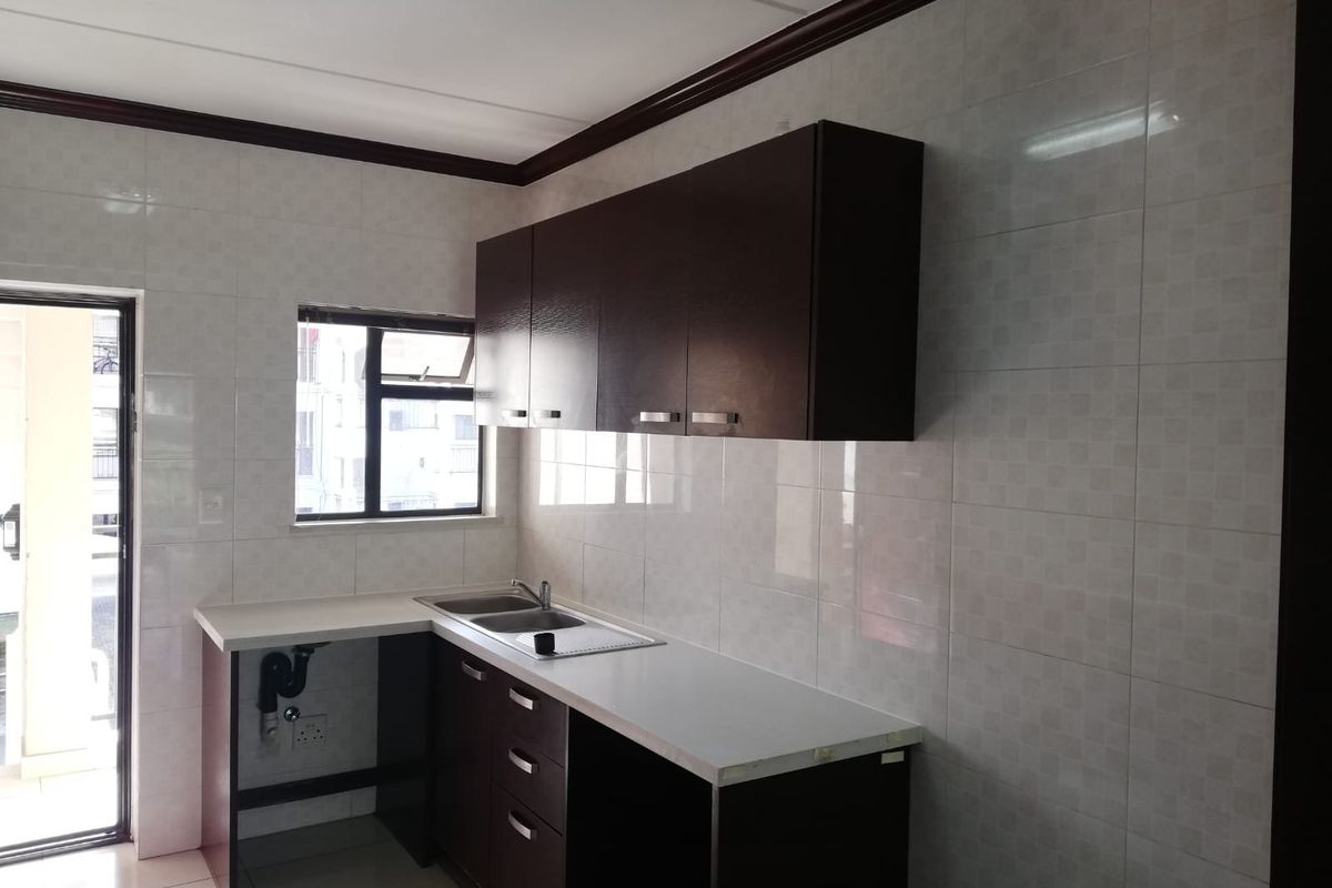 A functional kitchen featuring dark wood cabinetry, light laminate countertops, a stainless steel double sink, and full-height wall tiling.
