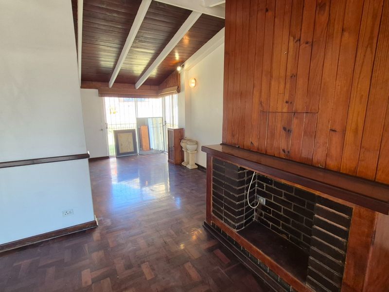 Spacious living area featuring a prominent brick fireplace, timber wall cladding, exposed beam ceilings, and traditional parquet flooring.