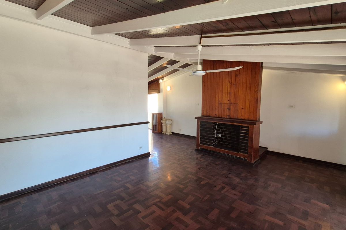 Spacious living area featuring dark parquet flooring, a central brick fireplace, and exposed timber ceiling beams.