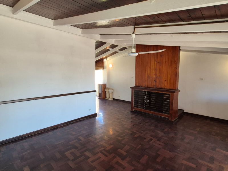 Spacious living area featuring dark parquet flooring, a central brick fireplace, and exposed timber ceiling beams.