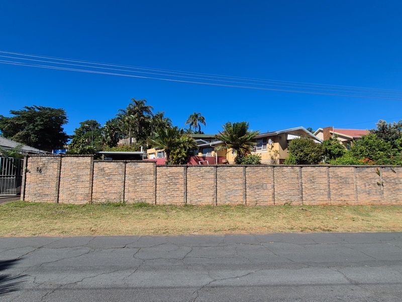 Street view of the property featuring a prominent brick boundary wall, metal entrance gate, and paved driveway leading to the residence.