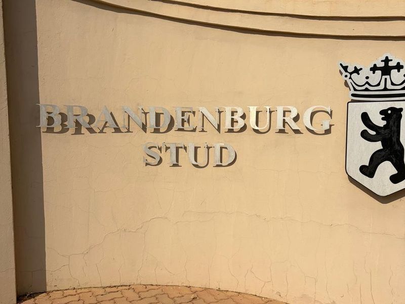 Entrance signage for Brandenburg Stud featuring a curved boundary wall with electric fencing and paved driveway access.