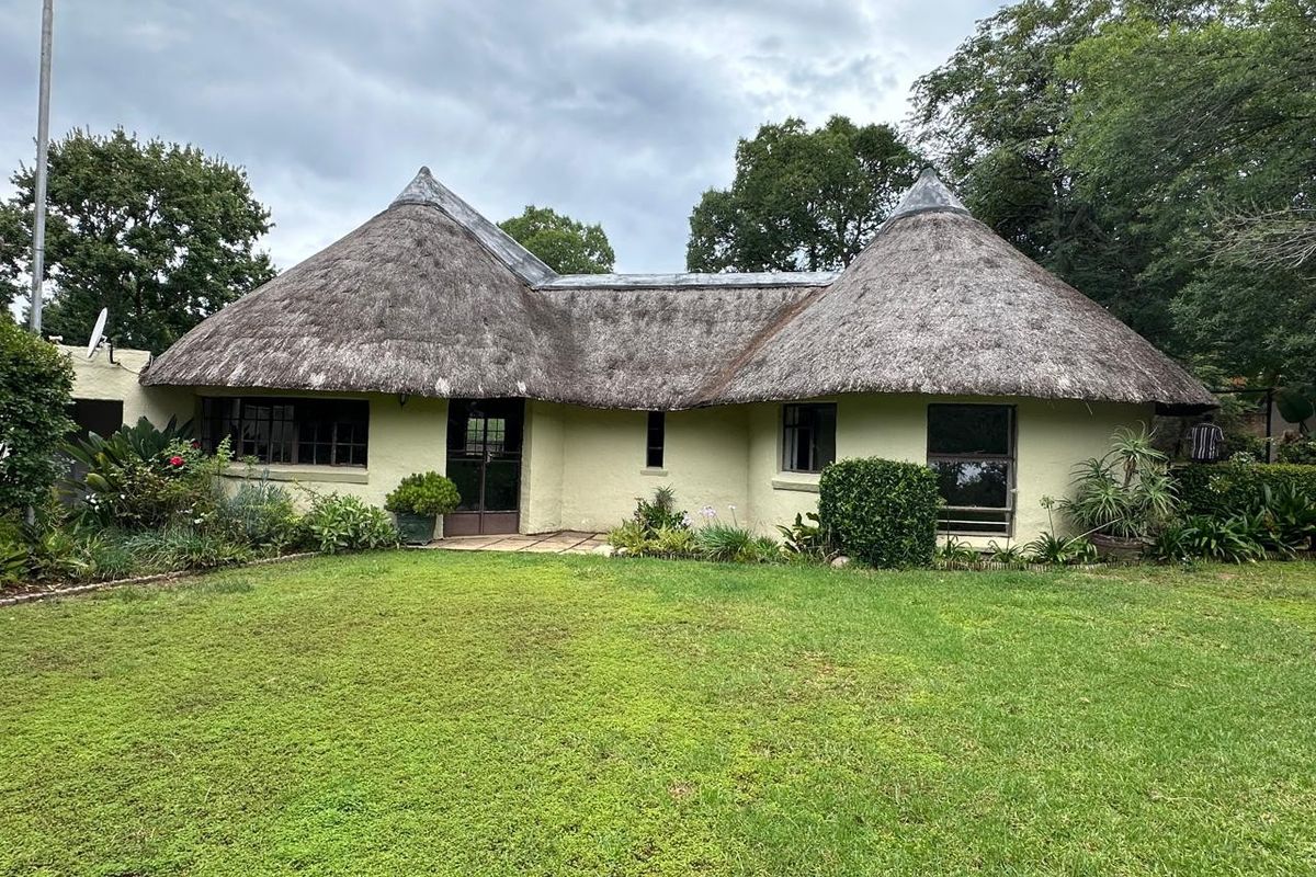 A charming farm-style cottage featuring a traditional thatched roof, plastered exterior walls, and a surrounding garden with a paved patio entrance.