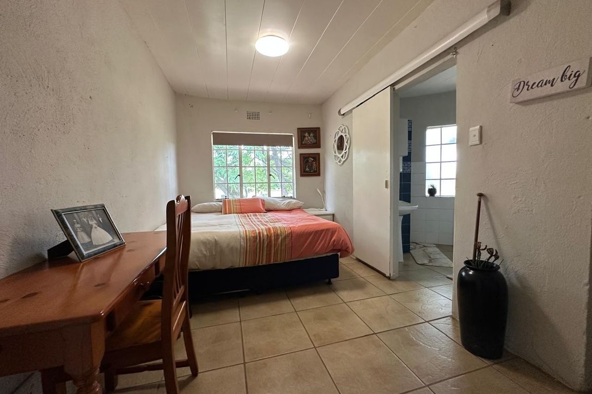 A bedroom featuring tiled flooring, a sliding door leading to an en-suite bathroom, and a window providing natural light.