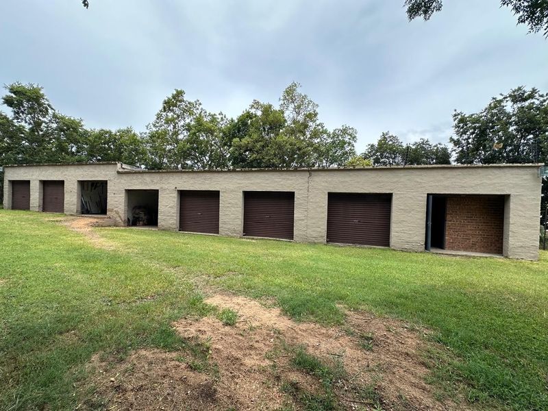 A long, multi-bay garage structure featuring several roller shutter doors, set against a rural landscape with mature trees.