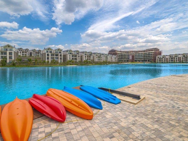A scenic view of a large artificial lagoon and waterfront paved area within a modern residential estate.