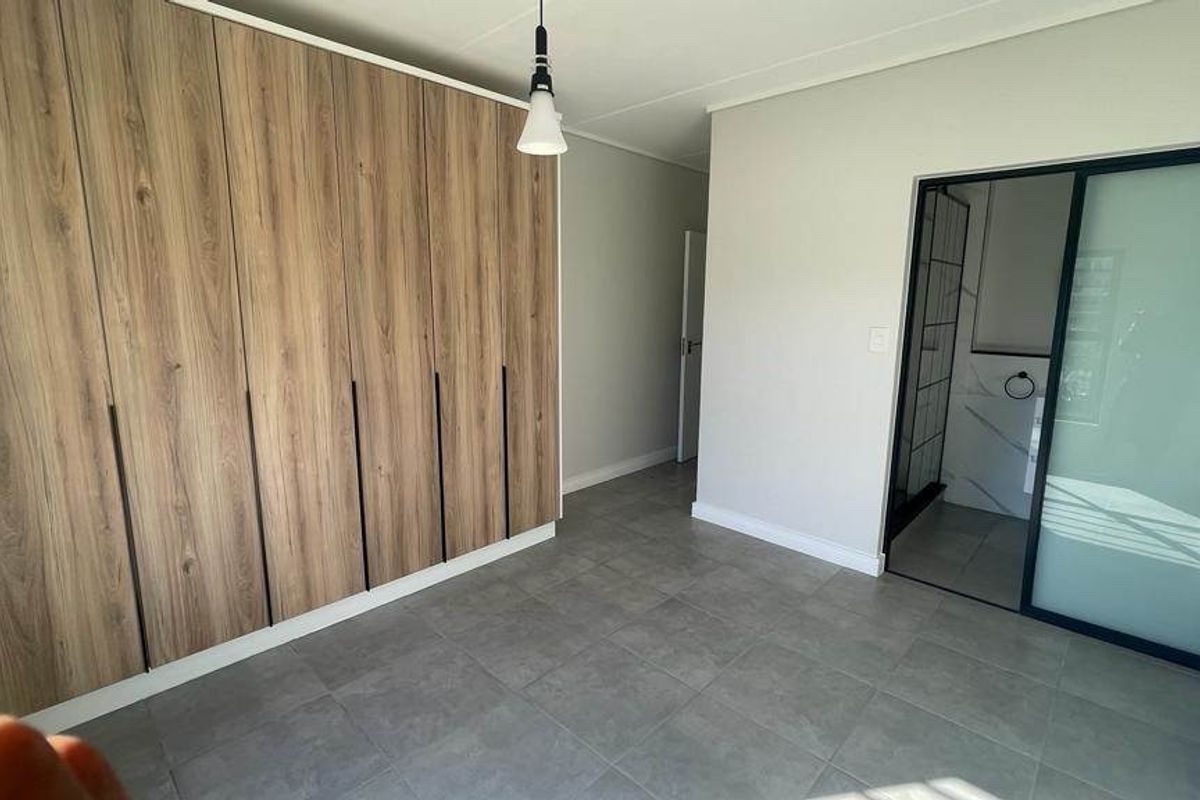Modern bedroom featuring extensive built-in wood-finish cupboards, neutral tiled flooring, and a sleek sliding door leading to an en-suite bathroom.