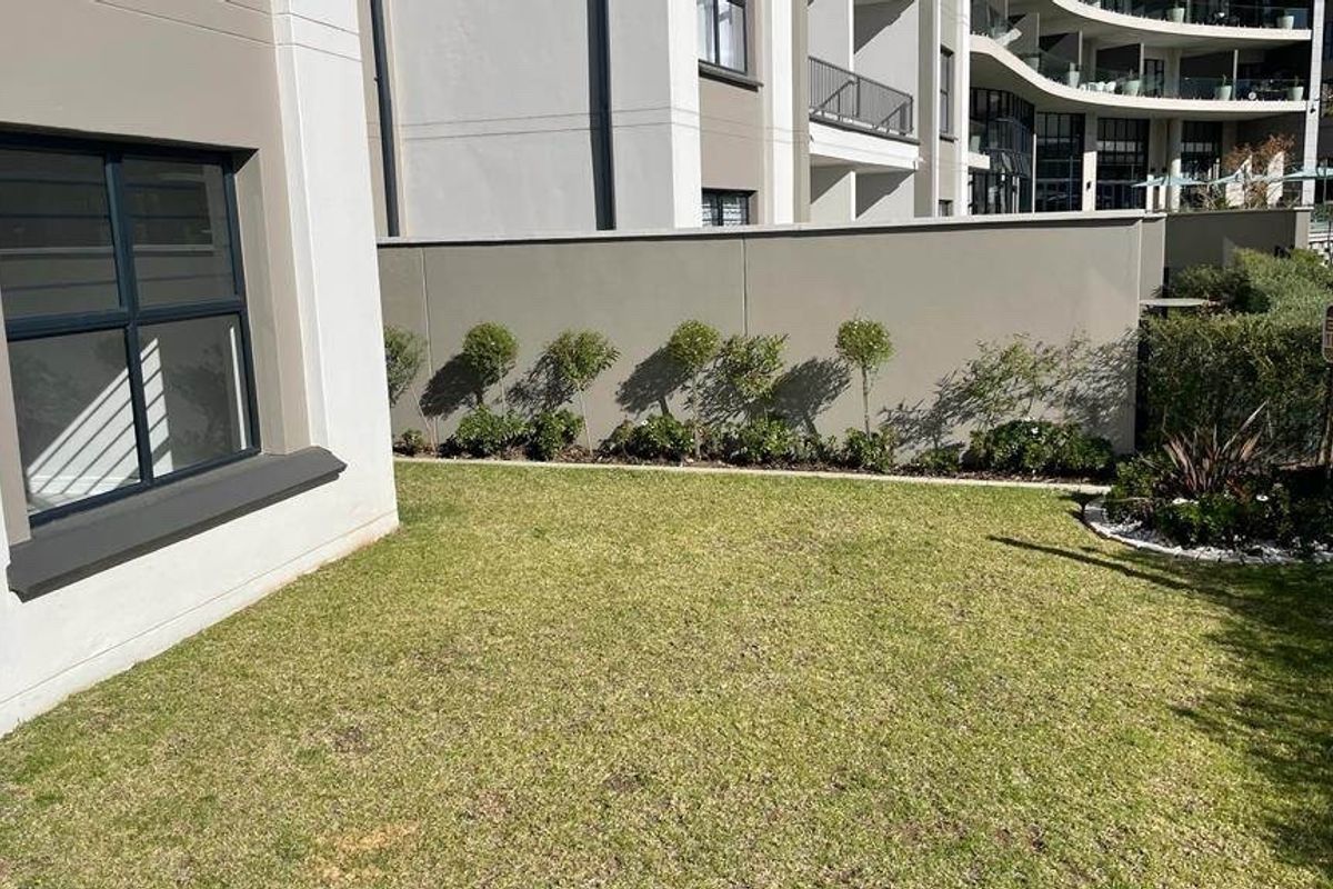 A well-maintained private rear garden area featuring a manicured lawn, boundary wall, and modern apartment building exterior.