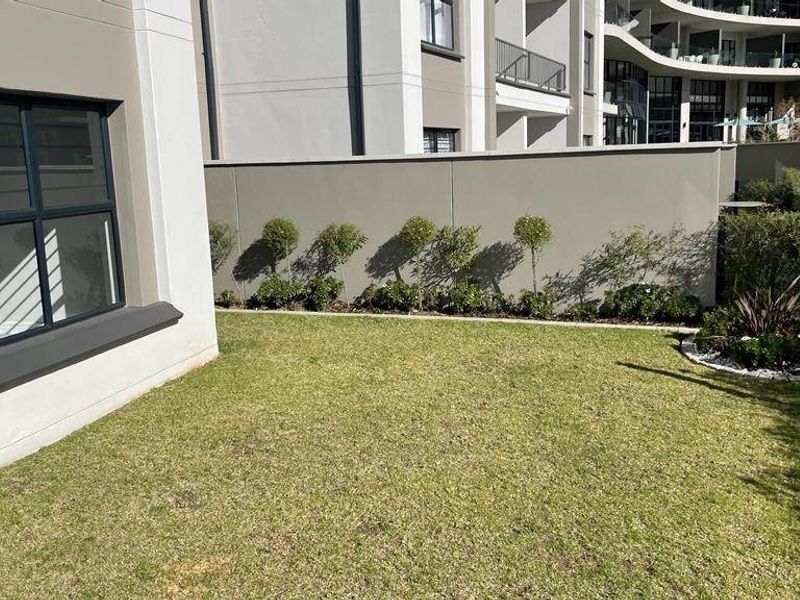 A well-maintained private rear garden area featuring a manicured lawn, boundary wall, and modern apartment building exterior.