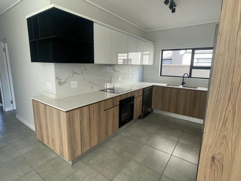 Modern kitchen featuring sleek wood-grain and white cabinetry, marble-look splashback, built-in oven, electric hob, and tiled flooring in a clean, contemporary layout.