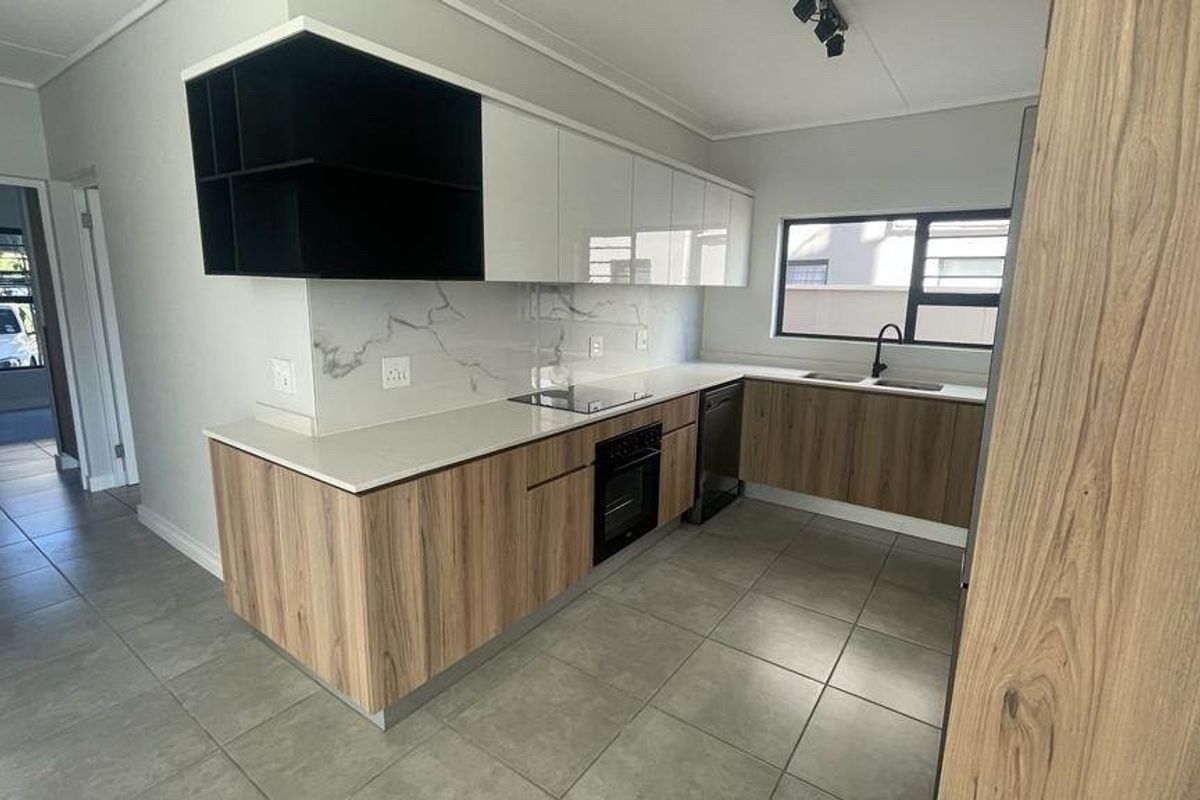 Modern kitchen featuring sleek wood-grain and white cabinetry, marble-look splashback, built-in oven, electric hob, and tiled flooring in a clean, contemporary layout.
