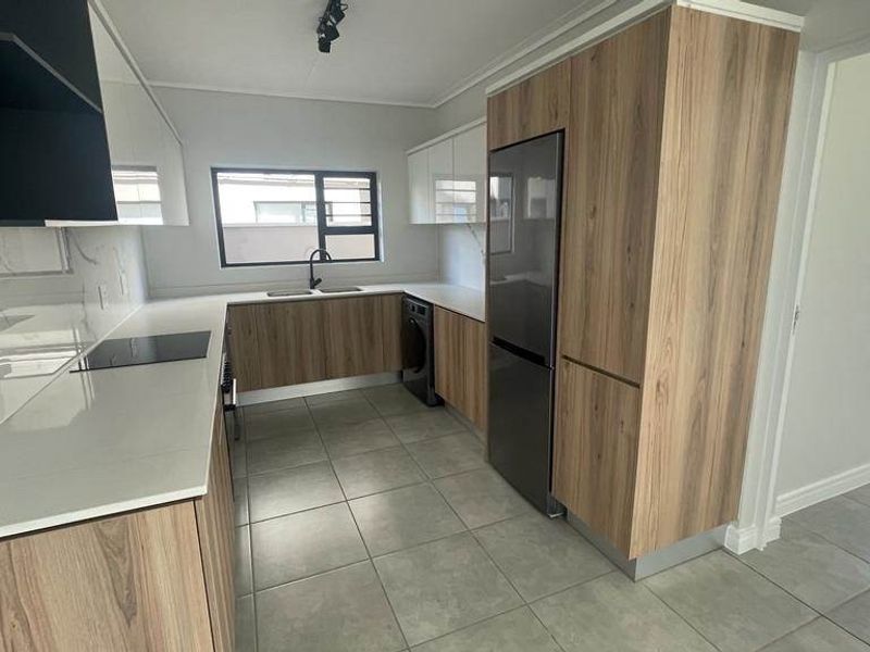 Modern kitchen featuring sleek wood-grain and white cabinetry, stone countertops, integrated appliances, and contemporary track lighting in a clean, open-plan layout.