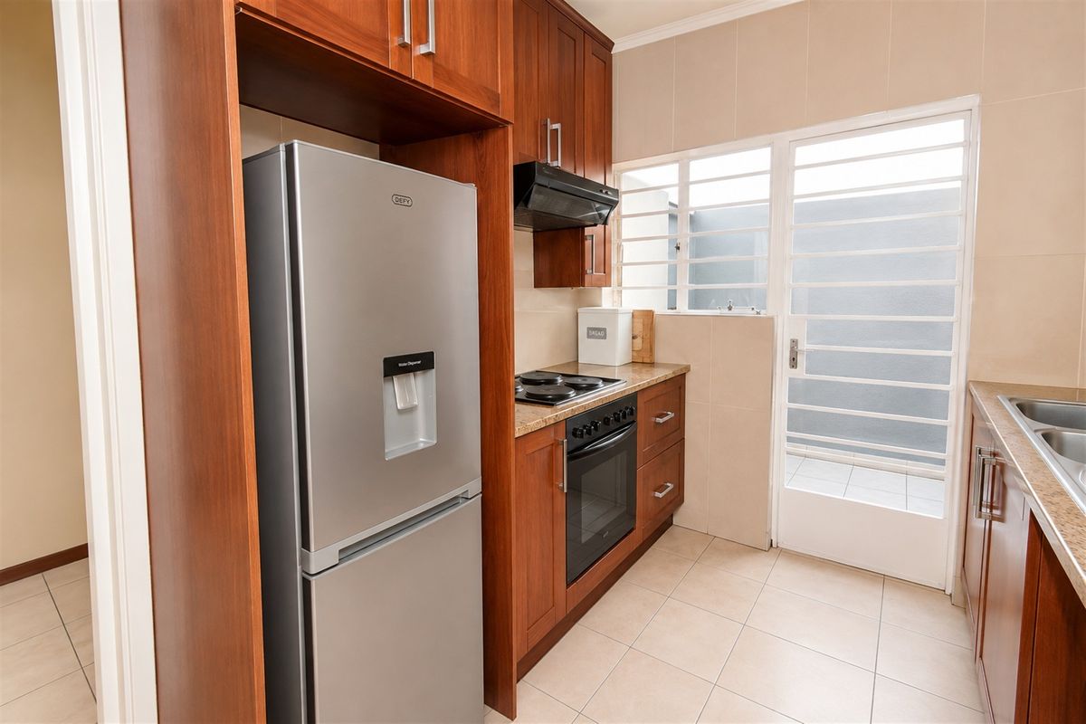 A functional kitchen featuring warm-toned wooden cabinetry, granite countertops, integrated appliances, and direct access to an outdoor area through a secure door.