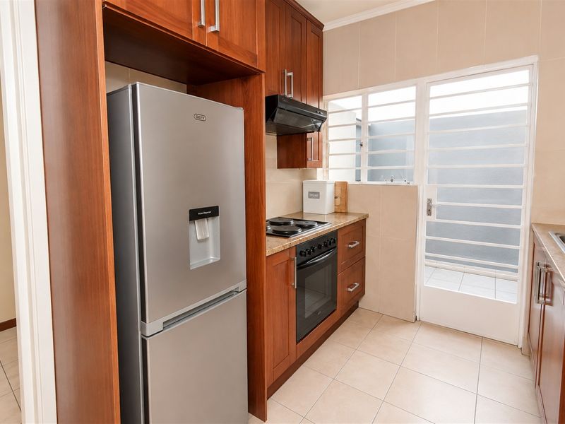A functional kitchen featuring warm-toned wooden cabinetry, granite countertops, integrated appliances, and direct access to an outdoor area through a secure door.