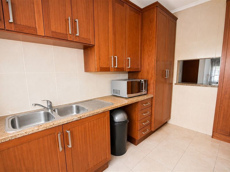 A functional scullery featuring wooden cabinetry, granite countertops, a double stainless steel sink, and a convenient serving hatch connecting to the adjacent room.