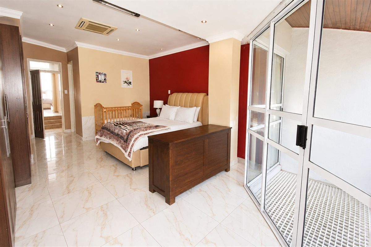Spacious bedroom featuring marble-look tiled flooring, recessed lighting, ducted air conditioning, and direct access to a private balcony through sliding glass doors.
