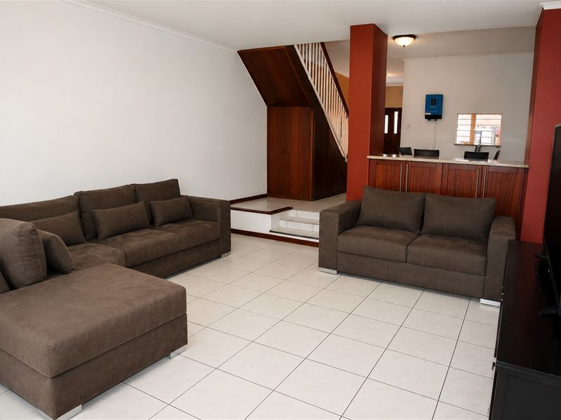 Open plan living area featuring tiled flooring, a wooden staircase, and a breakfast bar connecting to the kitchen space.