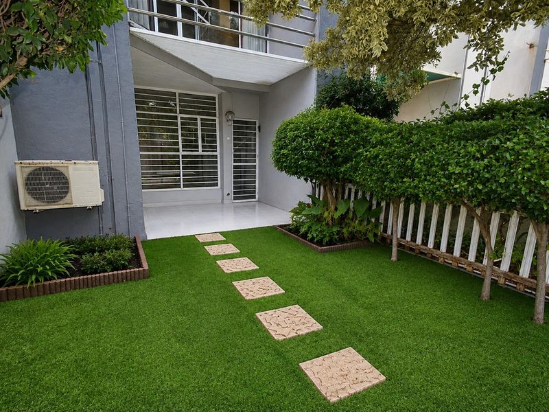 A well-maintained rear garden featuring artificial turf, a stone pathway, and a paved patio area leading to the townhouse entrance.