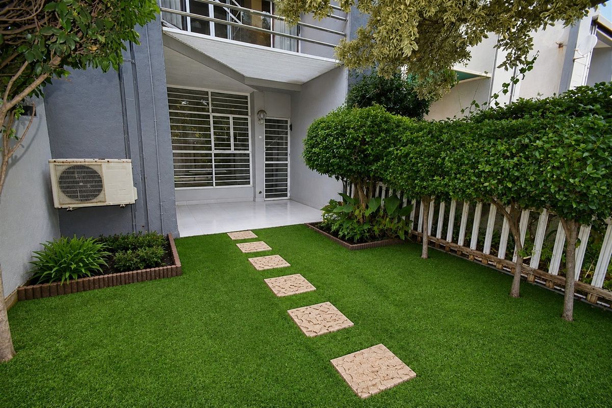 A well-maintained rear garden featuring artificial turf, a stone pathway, and a paved patio area leading to the townhouse entrance.