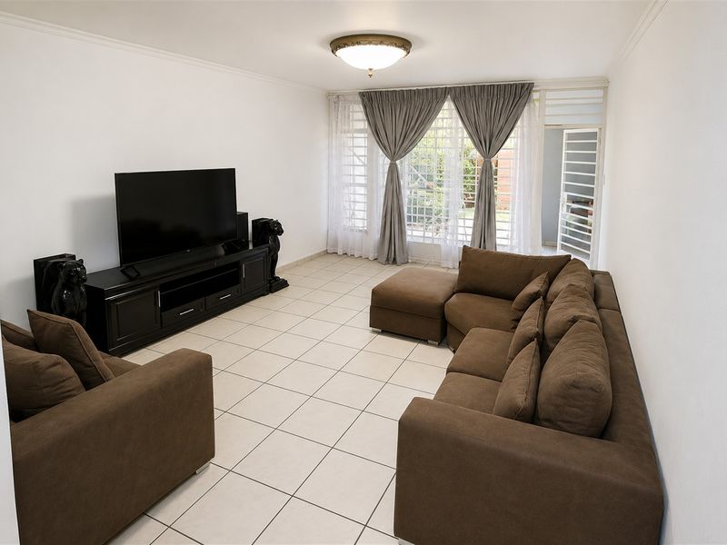 A spacious living room featuring neutral ceramic floor tiles, a flush mount ceiling light, and direct access to the outdoor area via a sliding glass door.