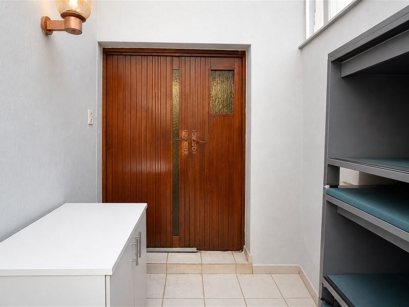 An entrance area featuring double wooden doors with glass inserts, tiled flooring, and a wall-mounted light fixture.